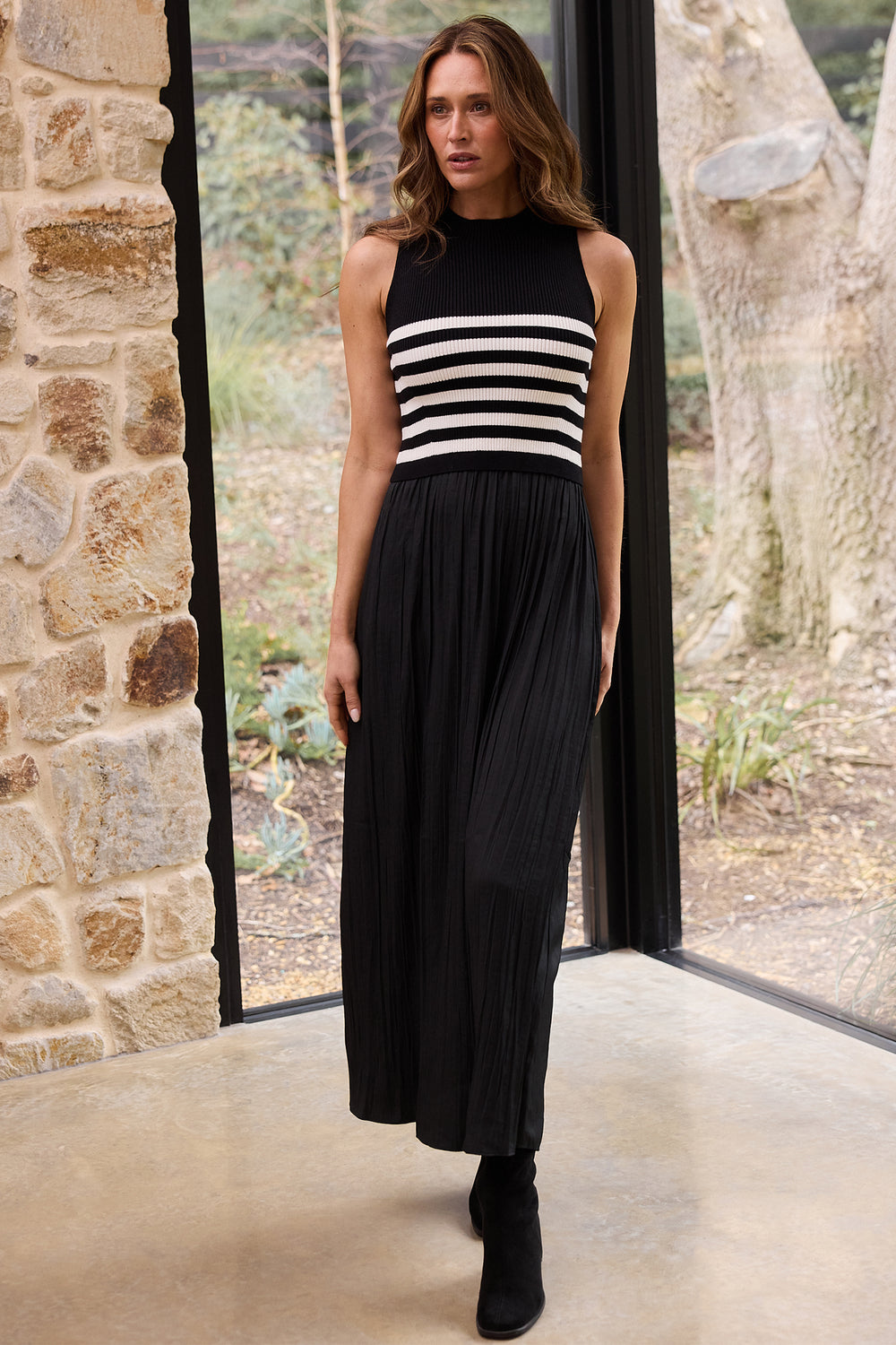 Woman wearing a black sleeveless dress with white stripes in a room with stone walls and large windows.