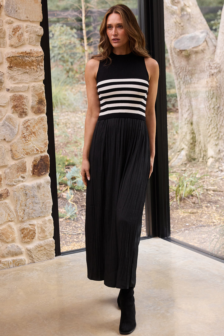Woman wearing a black sleeveless dress with white stripes in a room with stone walls and large windows.