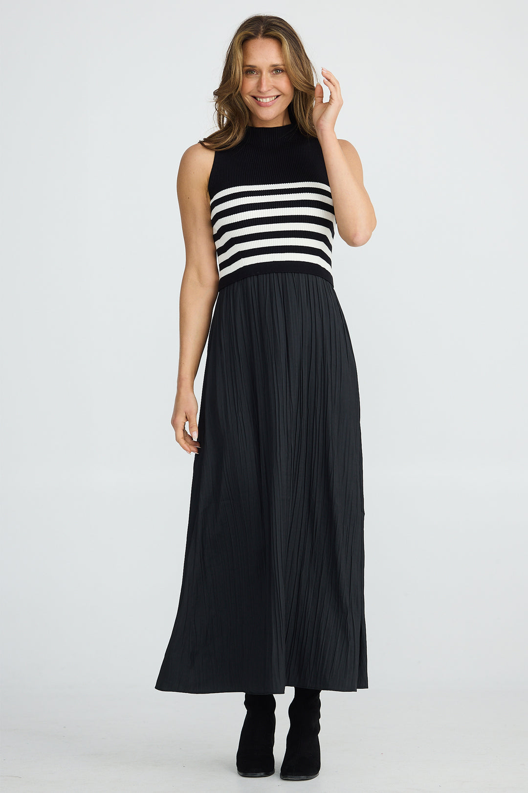 Woman wearing a black and white striped sleeveless top with a long black pleated skirt on a white background