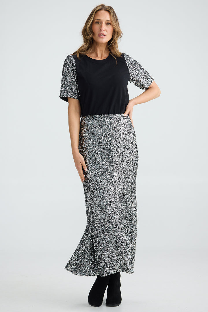 Woman wearing a black top with patterned sleeves and a long black and white patterned skirt on a light gray background