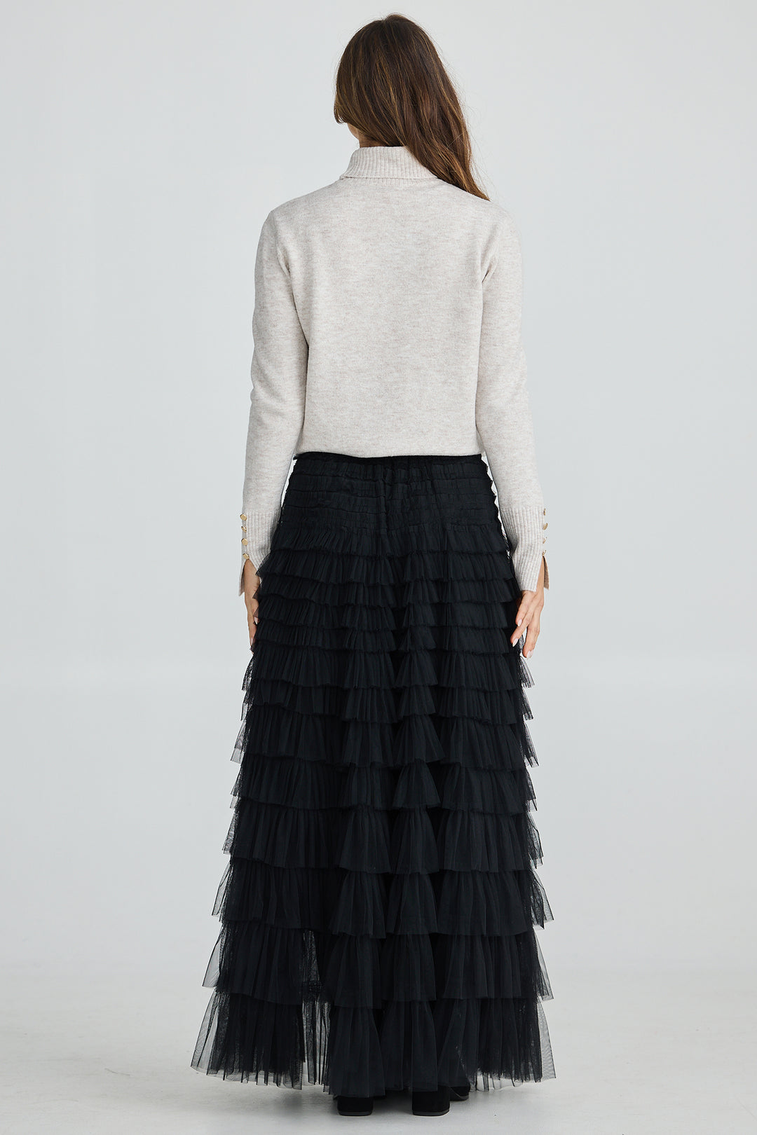 Woman wearing a long black tiered skirt and light gray sweater on a white background