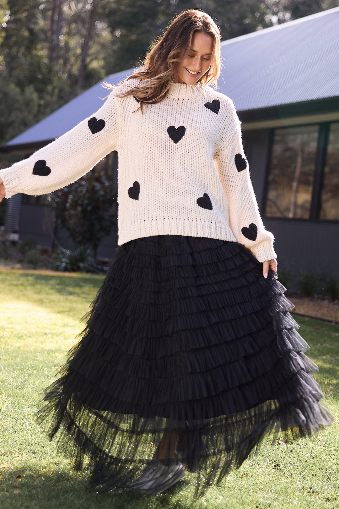 Woman wearing a white sweater with black heart patterns and a black tulle skirt outdoors.