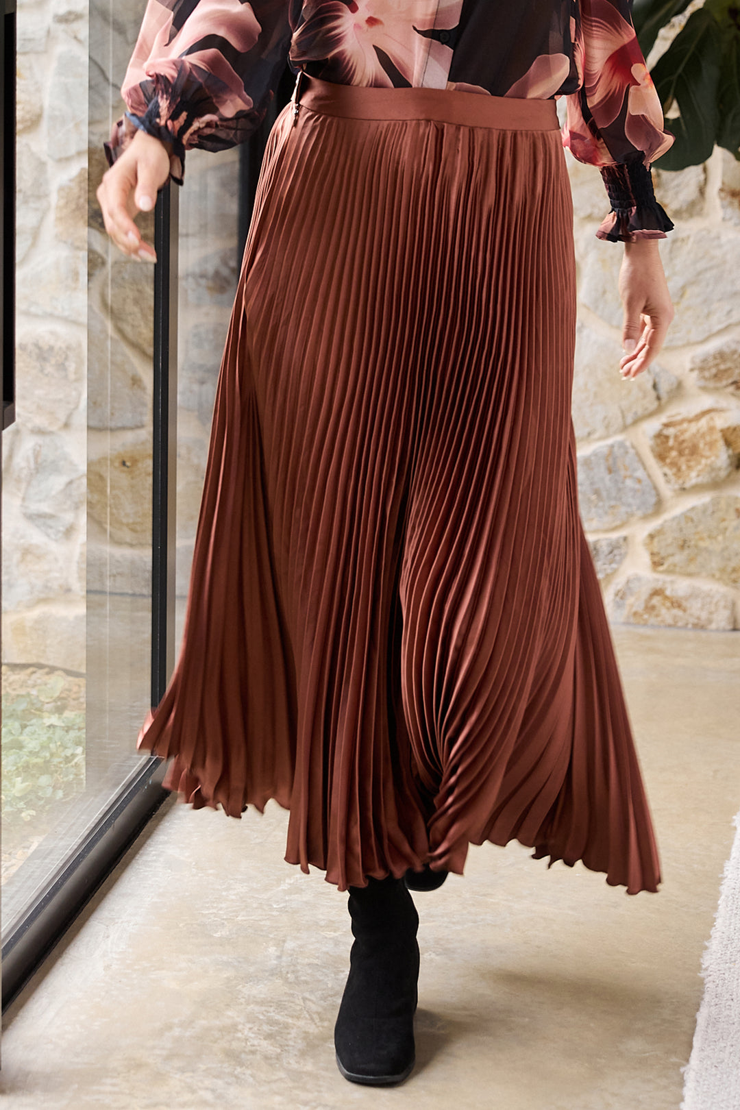 Person wearing a brown pleated skirt and black boots indoors.