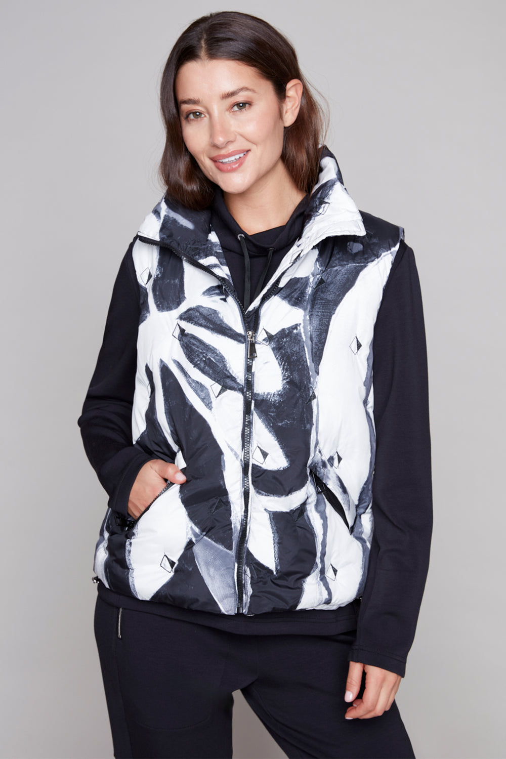 Woman wearing a black and white patterned vest over a black long-sleeve shirt on a gray background