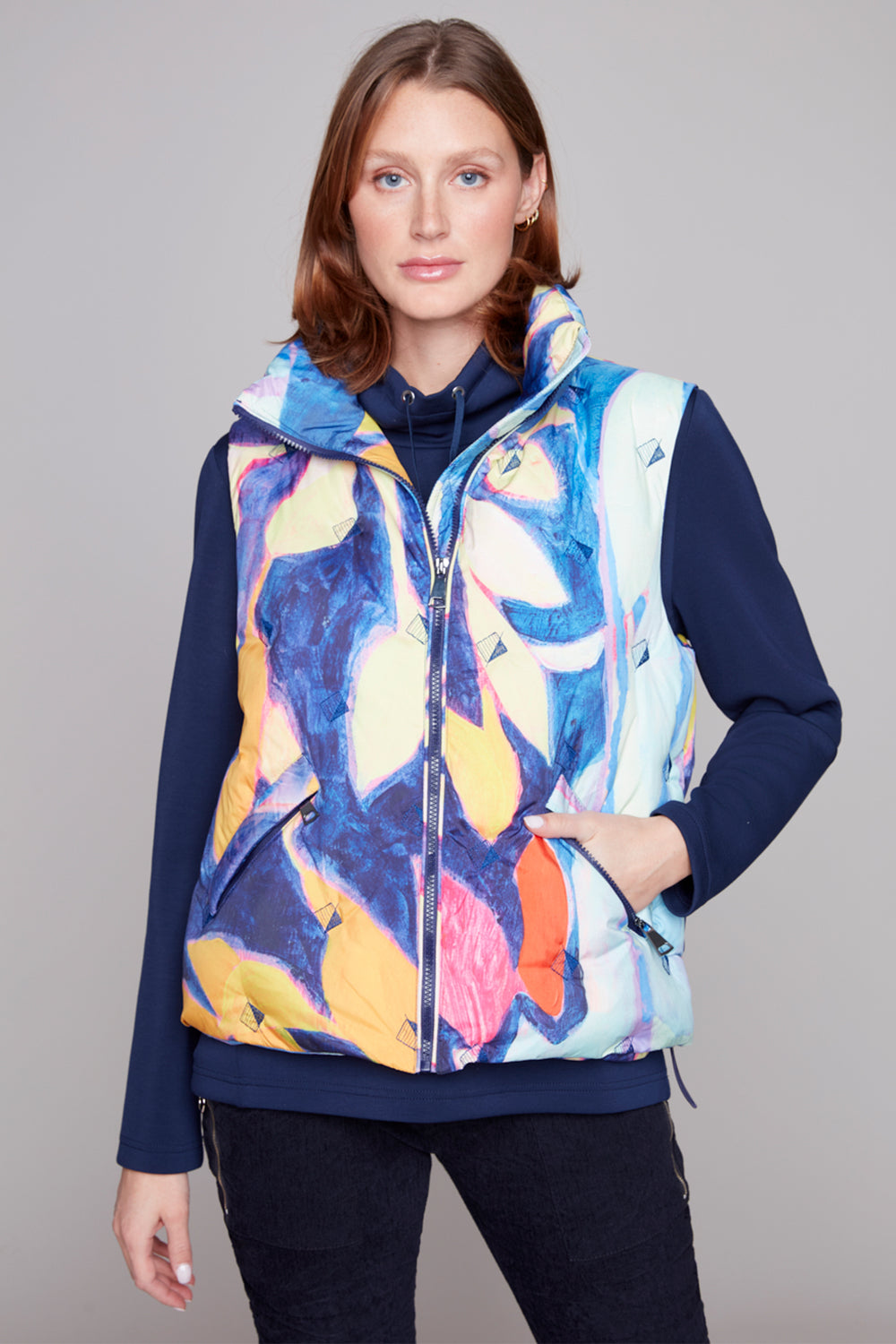 Woman wearing a colorful floral-patterned vest over a navy long-sleeve shirt on a gray background