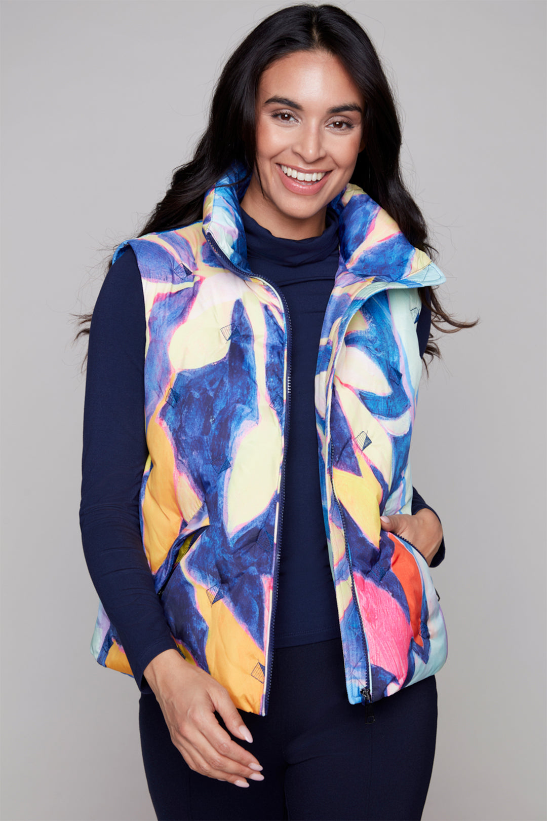 Woman wearing a colorful patterned vest over a dark outfit on a plain background