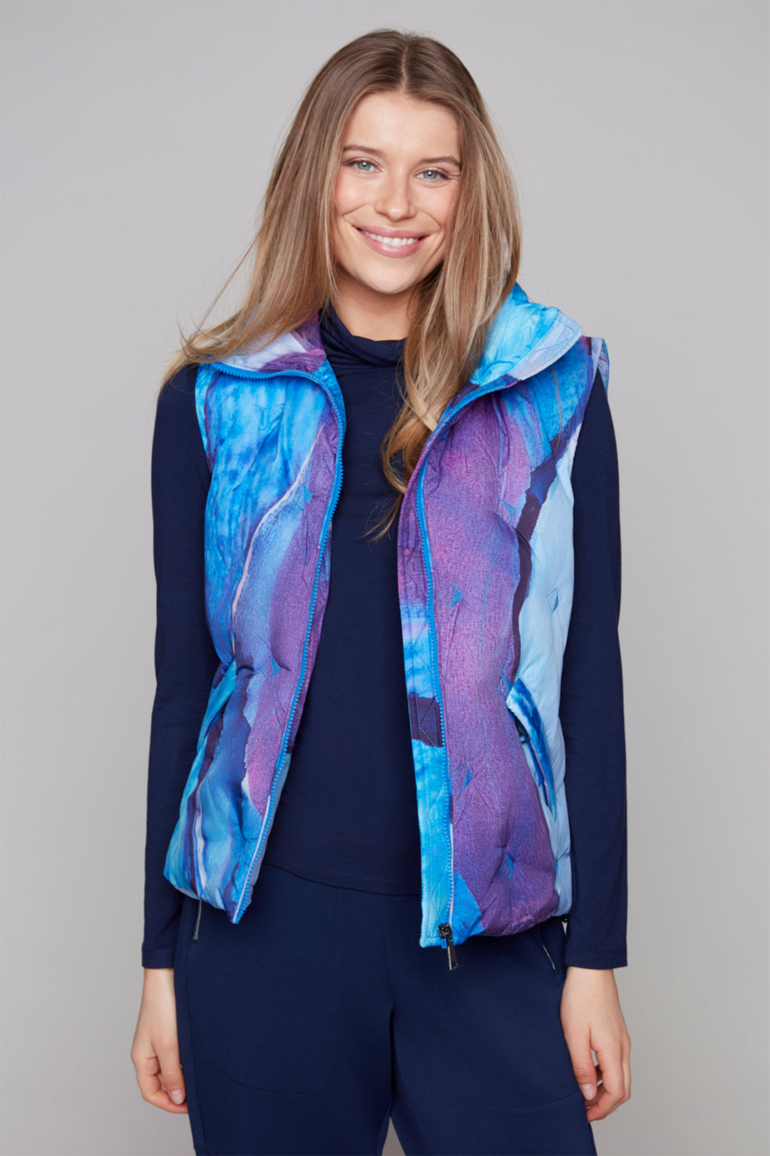 Woman wearing a blue and purple patterned vest over a navy outfit on a gray background