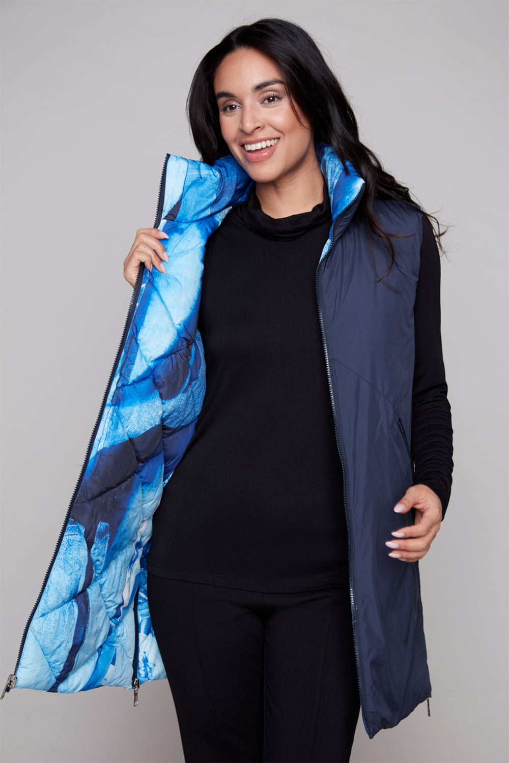 Woman wearing a blue patterned vest over a black outfit on a gray background