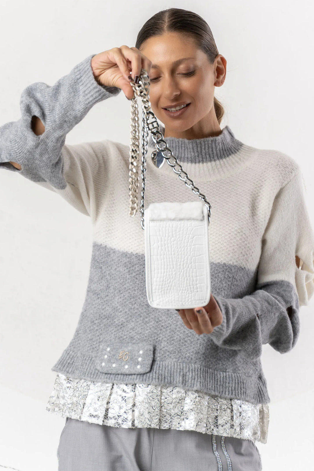Woman wearing a gray and white sweater holding a white handbag with a chain strap.