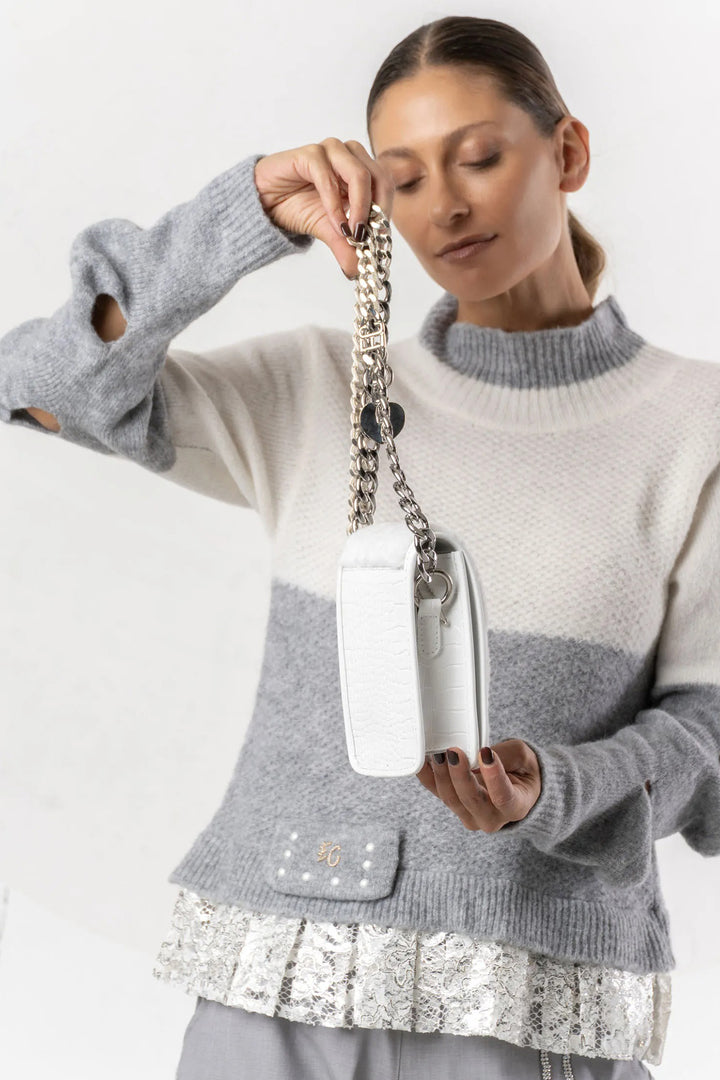 Woman holding a white handbag with a chain strap against a plain background