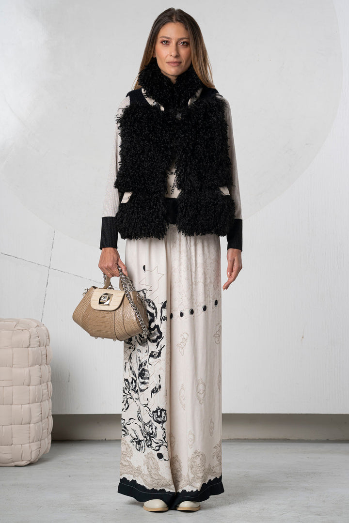 Woman wearing a black and white outfit with a fur vest, holding a beige handbag.