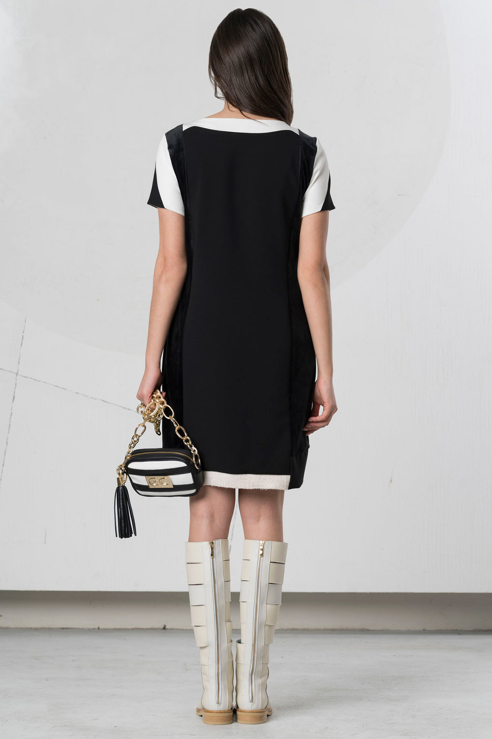 Woman wearing a black and white dress with knee-high boots, holding a striped handbag.