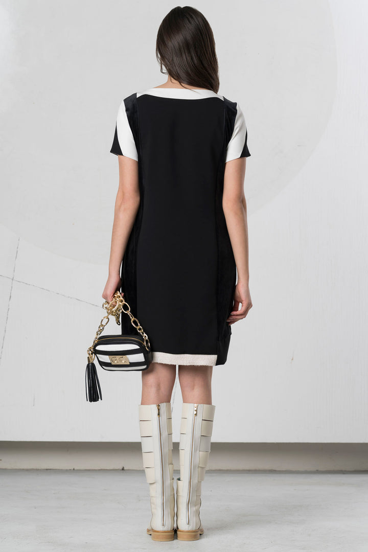 Woman wearing a black and white dress with knee-high boots, holding a striped handbag.