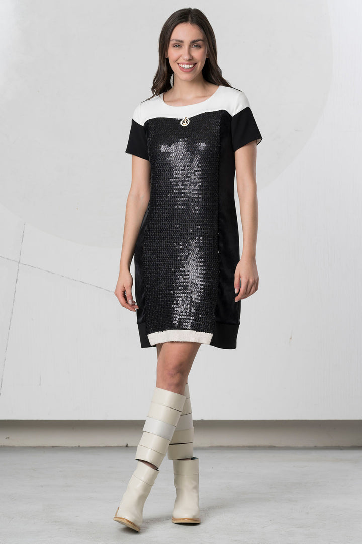 Woman wearing a black and white dress with sequin details on a plain background