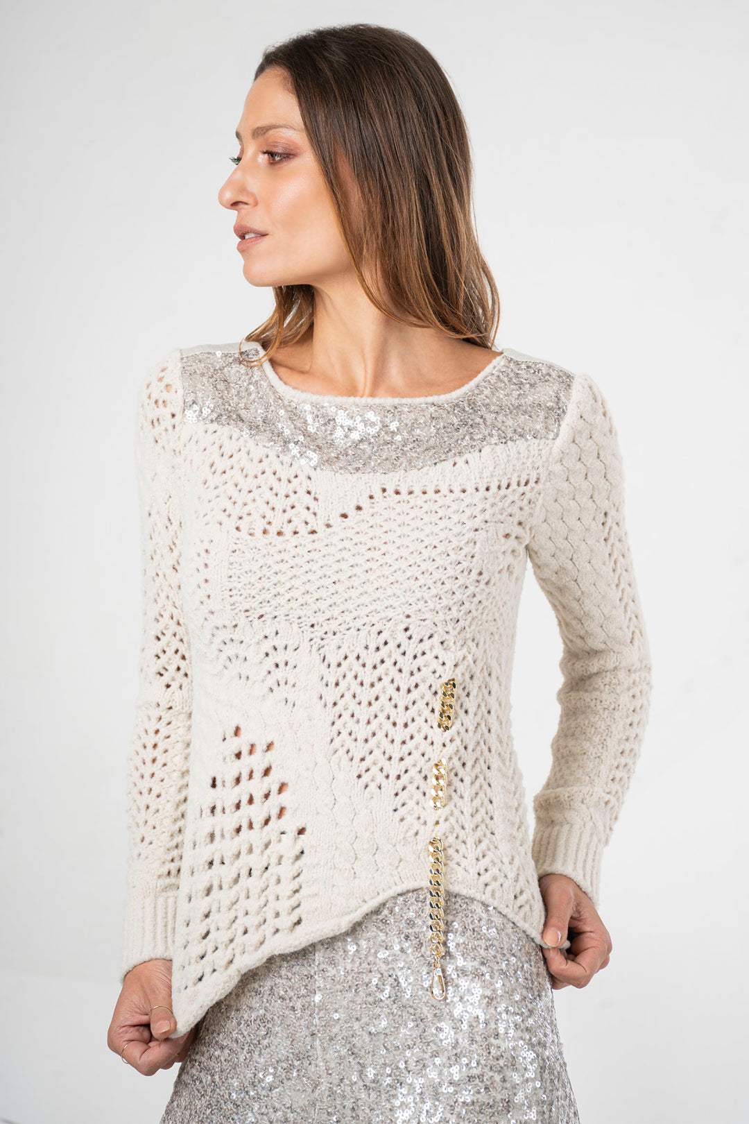 Woman wearing a cream-colored sweater with sequin details on a white background