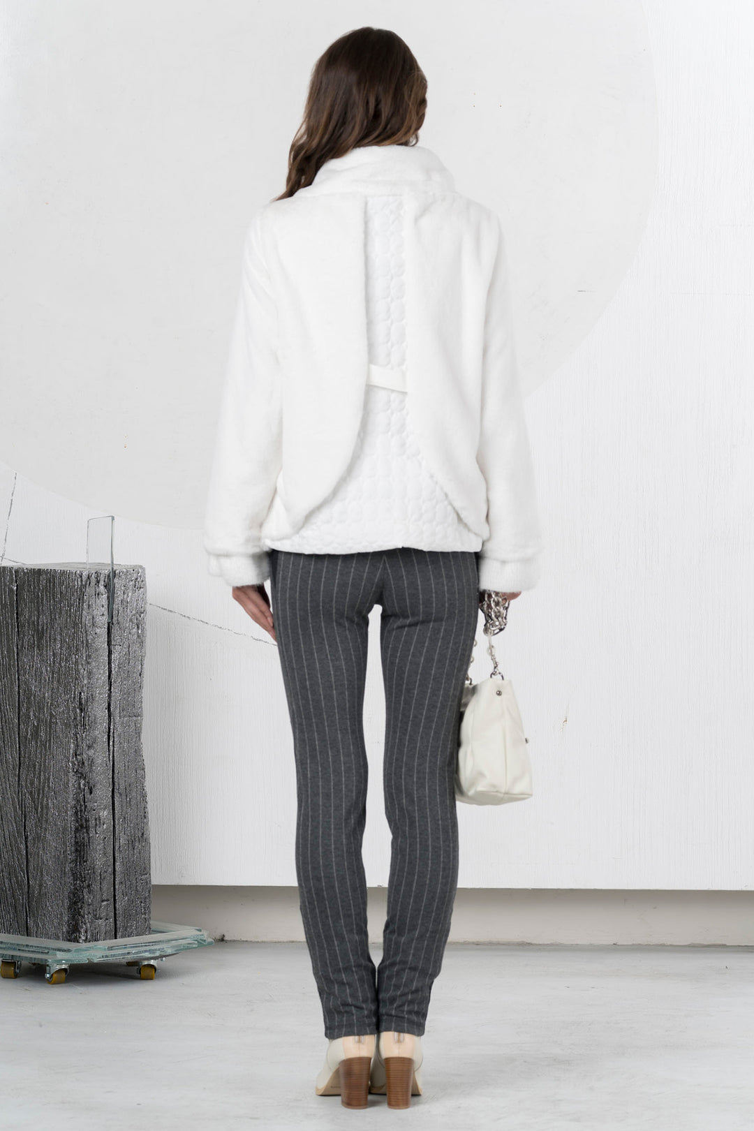 Woman wearing a white jacket and gray pinstripe pants in an indoor setting.