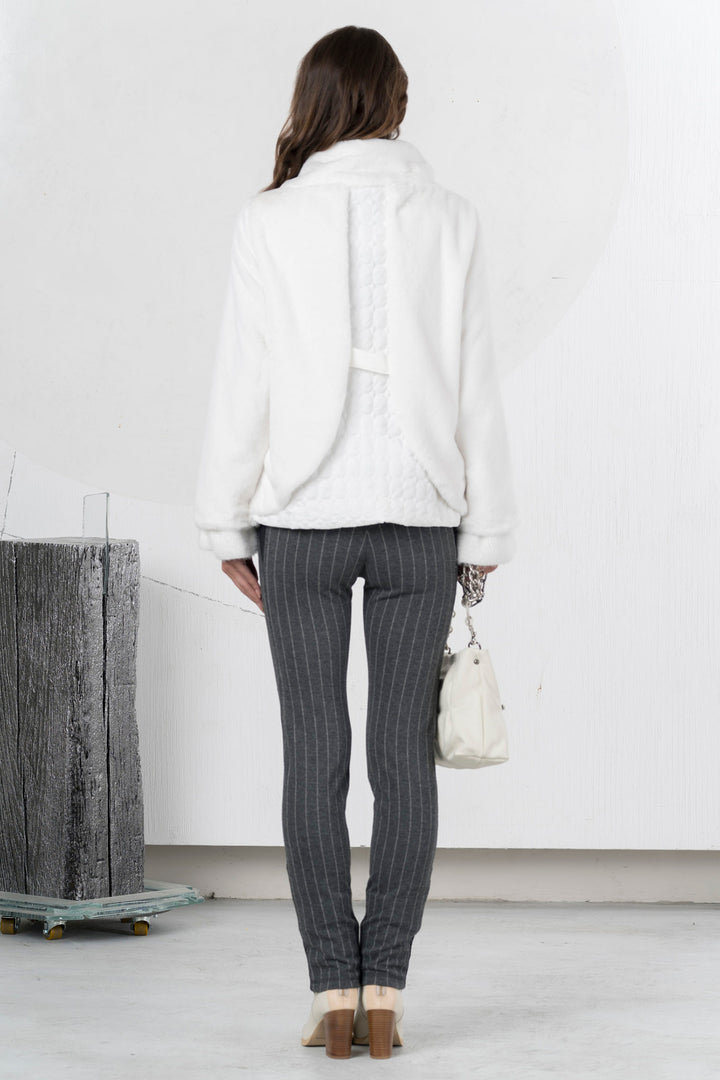 Woman wearing a white jacket and gray pinstripe pants in an indoor setting.