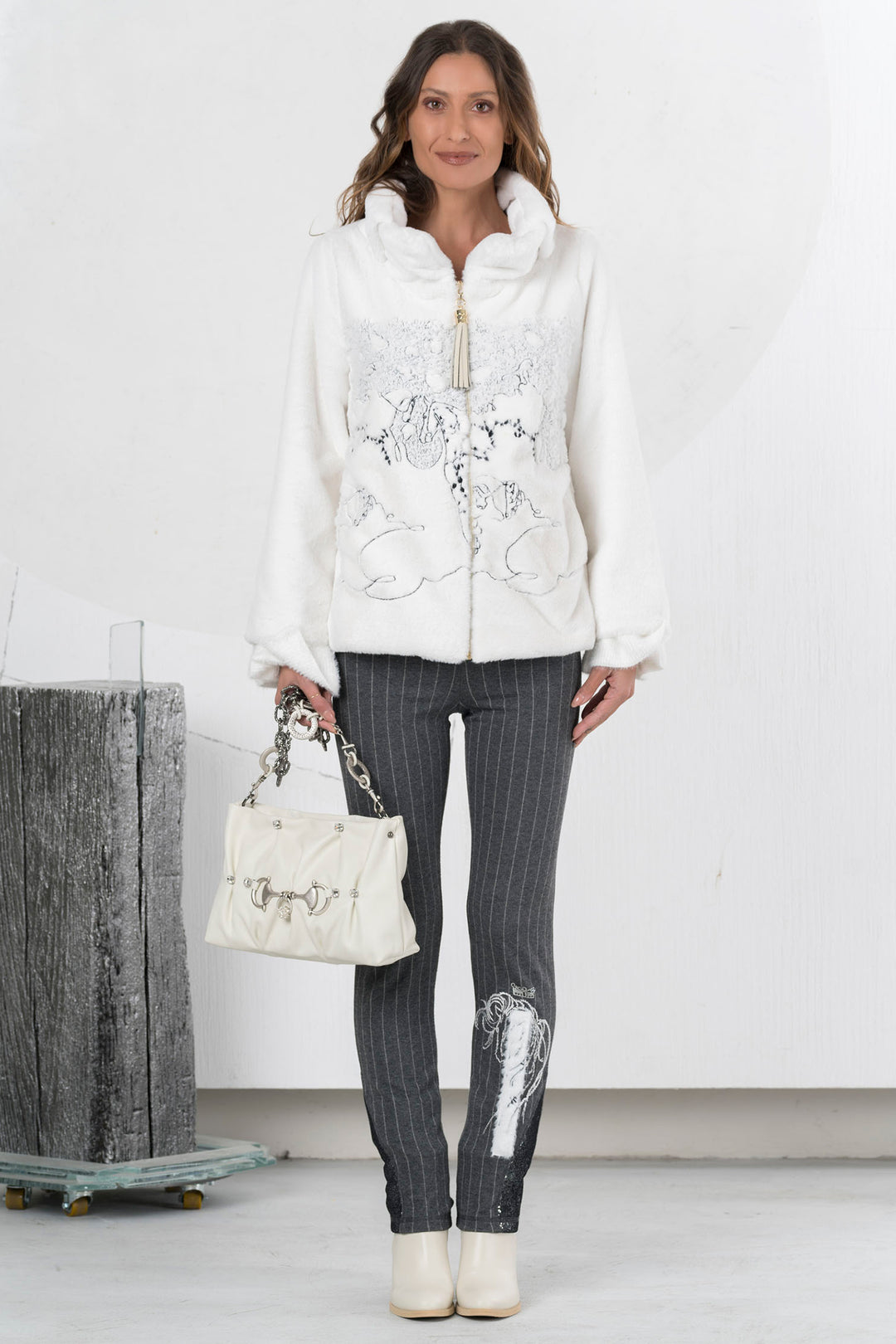 Woman wearing a white embroidered jacket and gray pinstripe pants, holding a matching handbag.