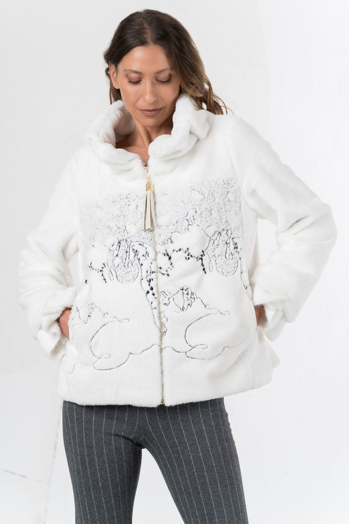 Woman wearing a white textured jacket with embroidered designs on a white background