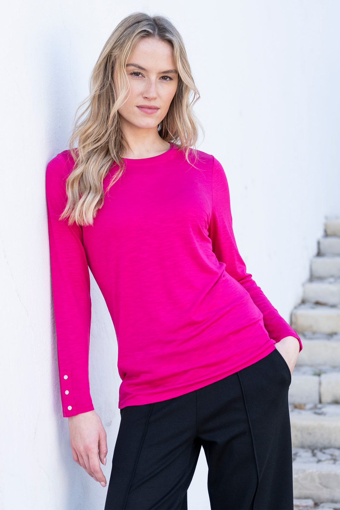 Woman wearing a bright pink long-sleeve top and black pants against a light background