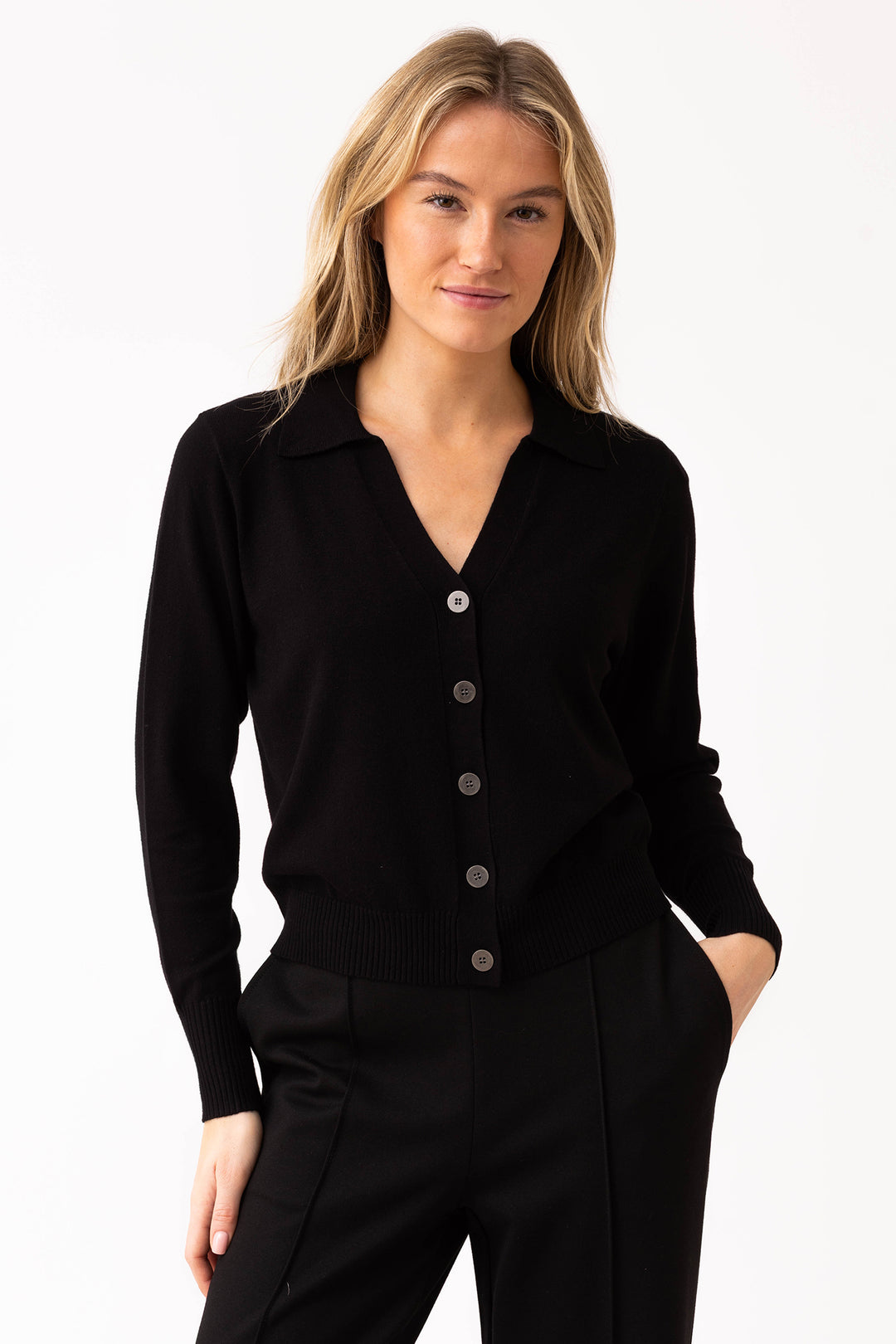 Woman wearing a black button-up cardigan and black pants on a white background