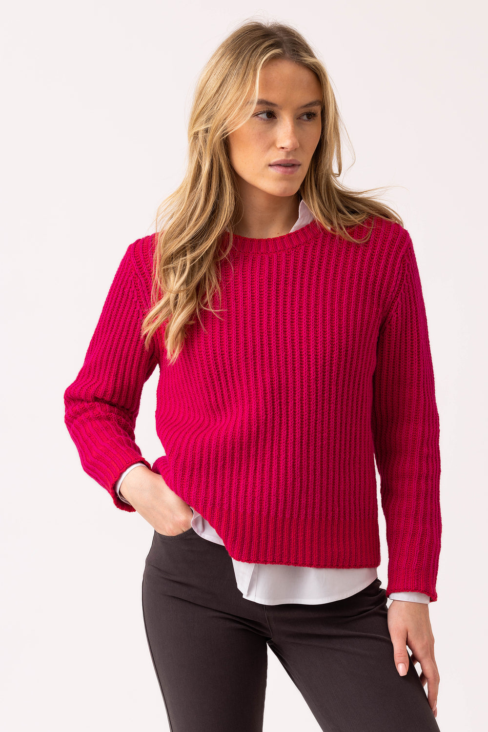 Woman wearing a bright pink sweater over a white shirt with black pants on a light gray background