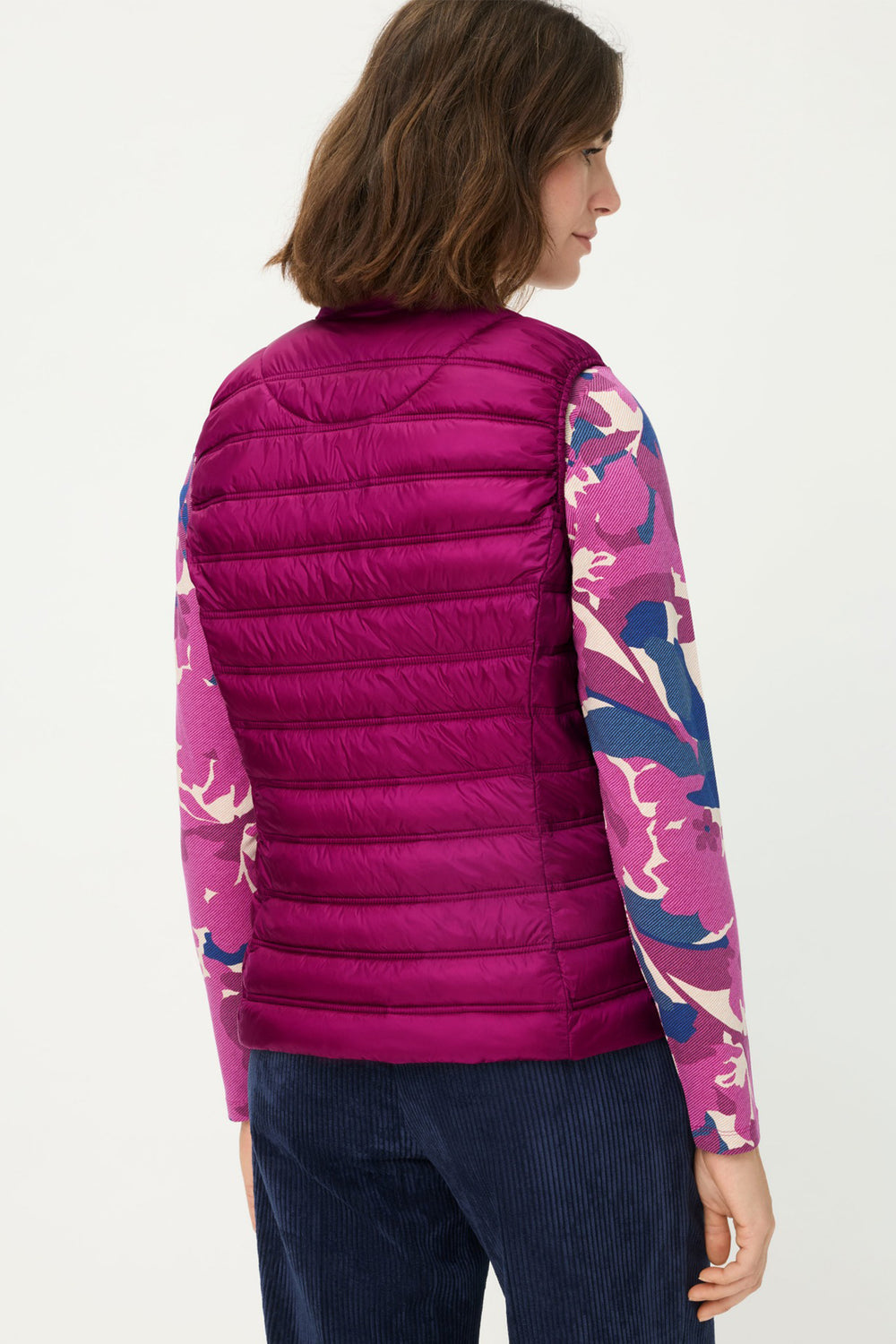 Person wearing a pink puffer vest over a colorful long-sleeve shirt on a white background