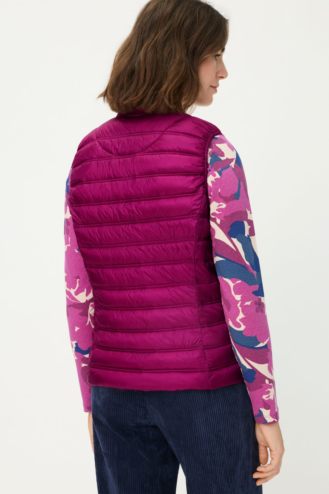 Person wearing a pink puffer vest over a colorful long-sleeve shirt on a white background