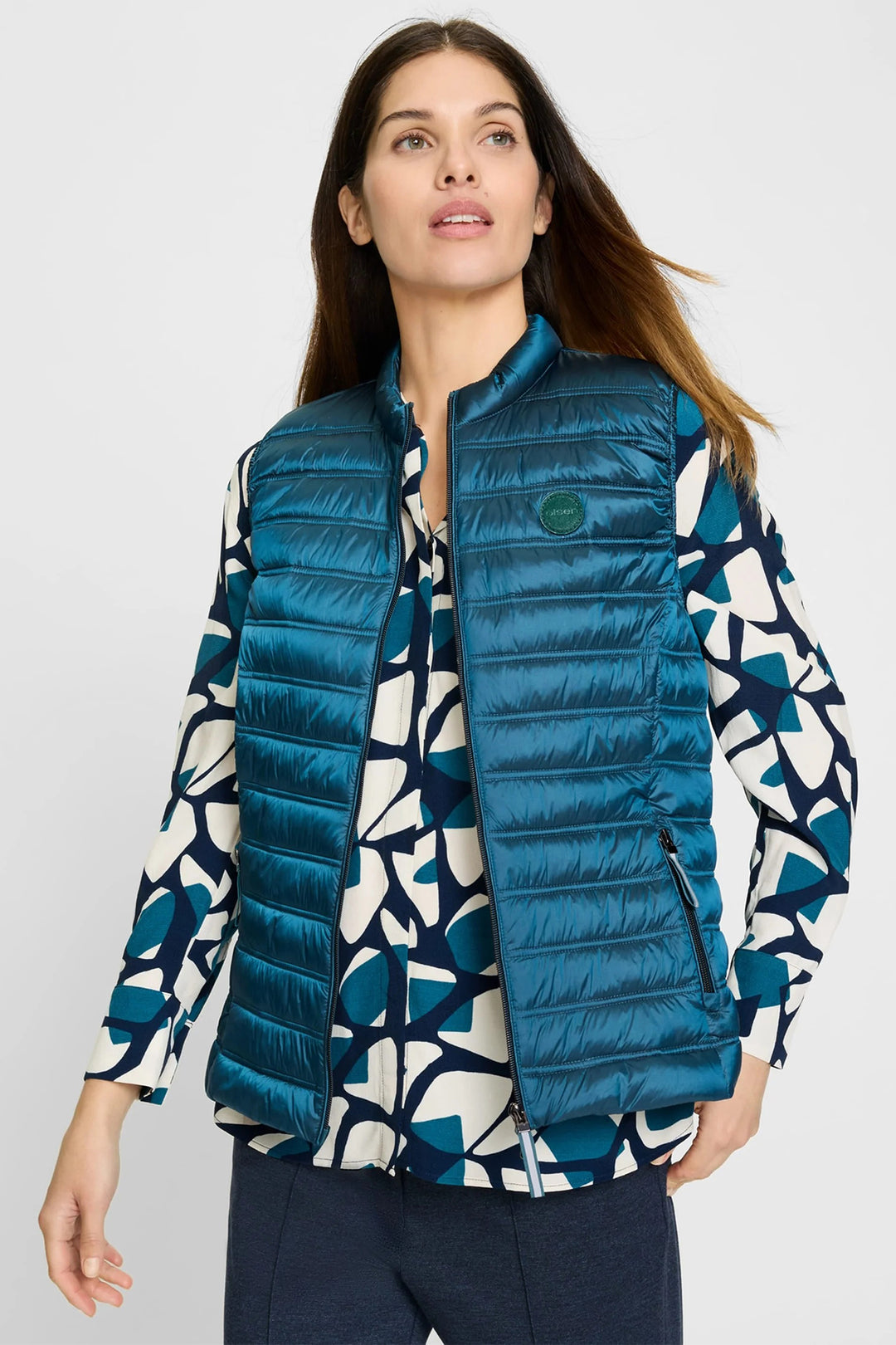 Woman wearing a blue puffer vest over a patterned shirt on a white background