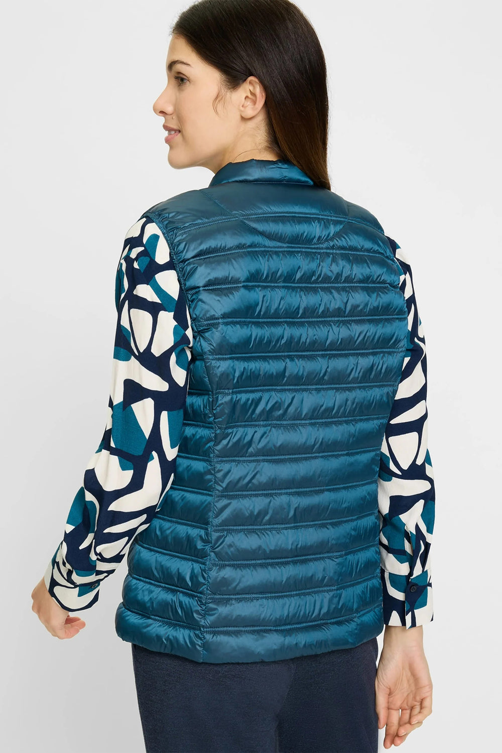 Woman wearing a blue puffer vest over a patterned shirt on a white background