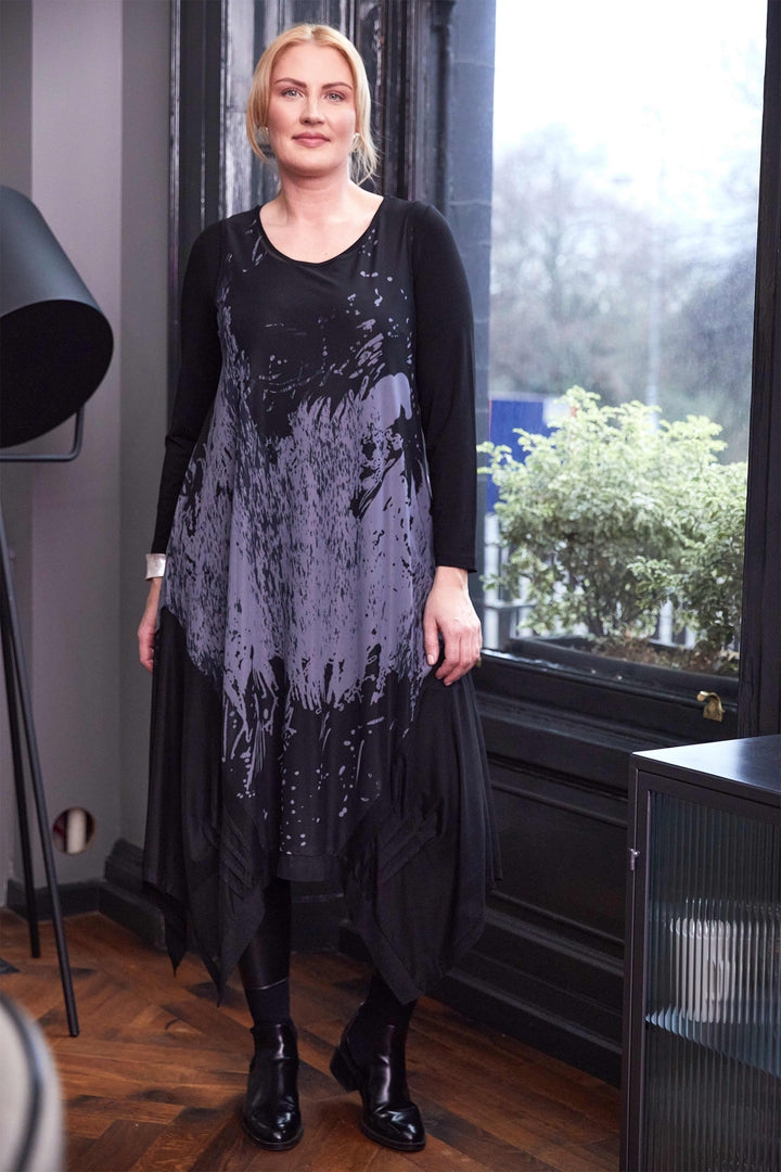 Woman wearing a black and gray dress standing indoors with a window in the background