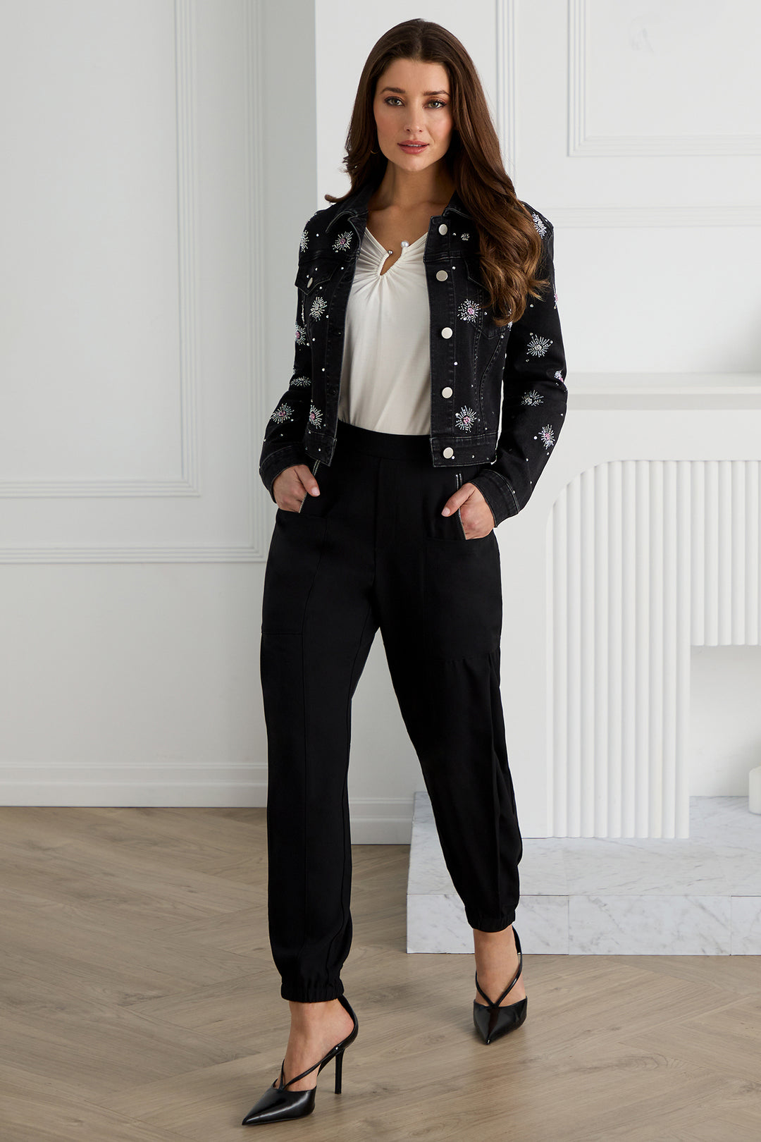 Woman wearing a black floral jacket, white blouse, and black pants in a minimalistic setting.