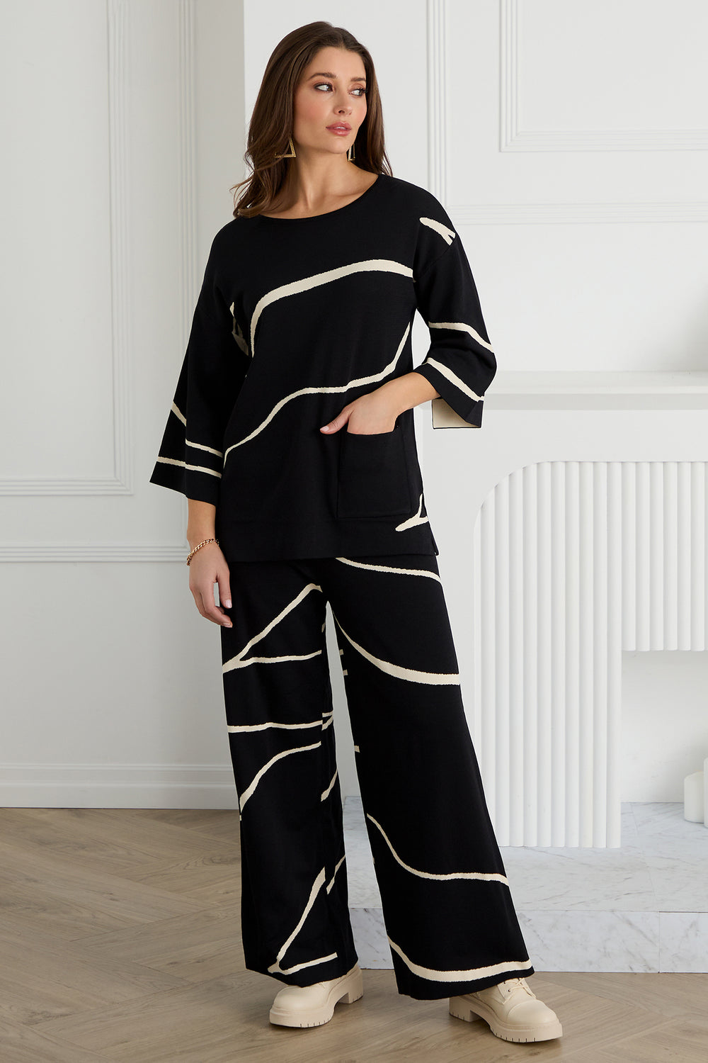 Woman wearing a black outfit with white patterns in a room with white walls and wooden floor.