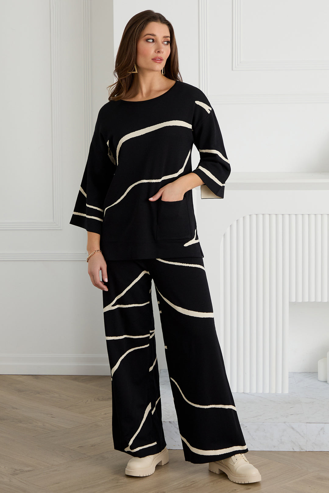 Woman wearing a black outfit with white patterns in a room with white walls and wooden floor.