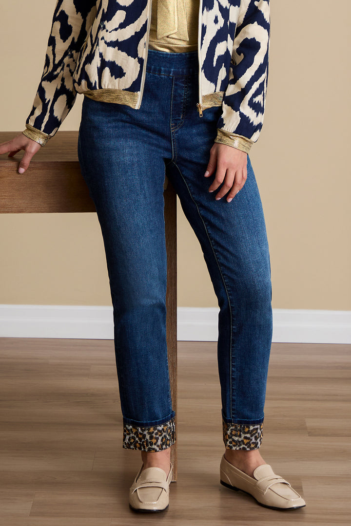 Person wearing blue jeans with leopard print cuffs and a patterned jacket on a wooden floor.