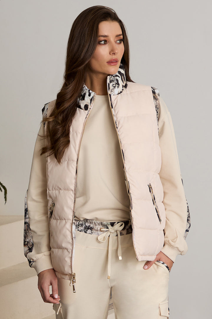 Woman wearing a beige puffer jacket with black and white patterned accents on a plain background