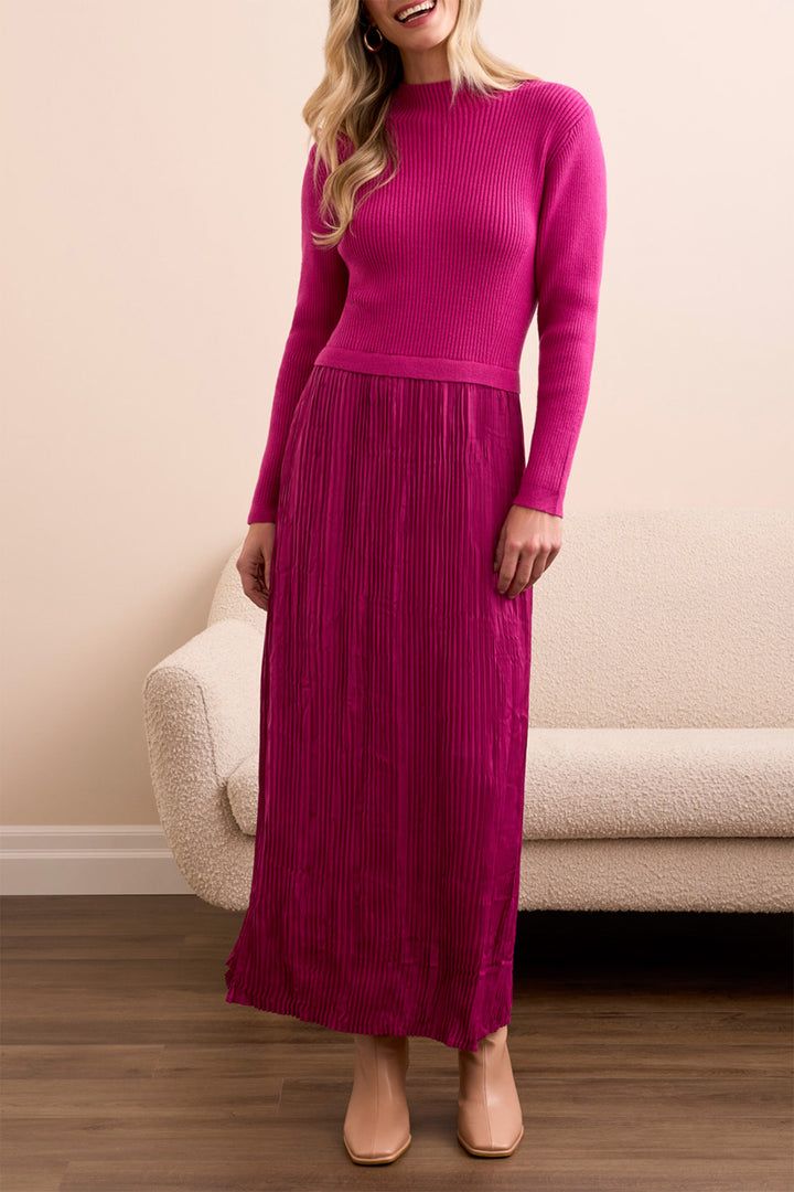 Woman wearing a pink ribbed sweater and pleated skirt standing in a room with a beige sofa.