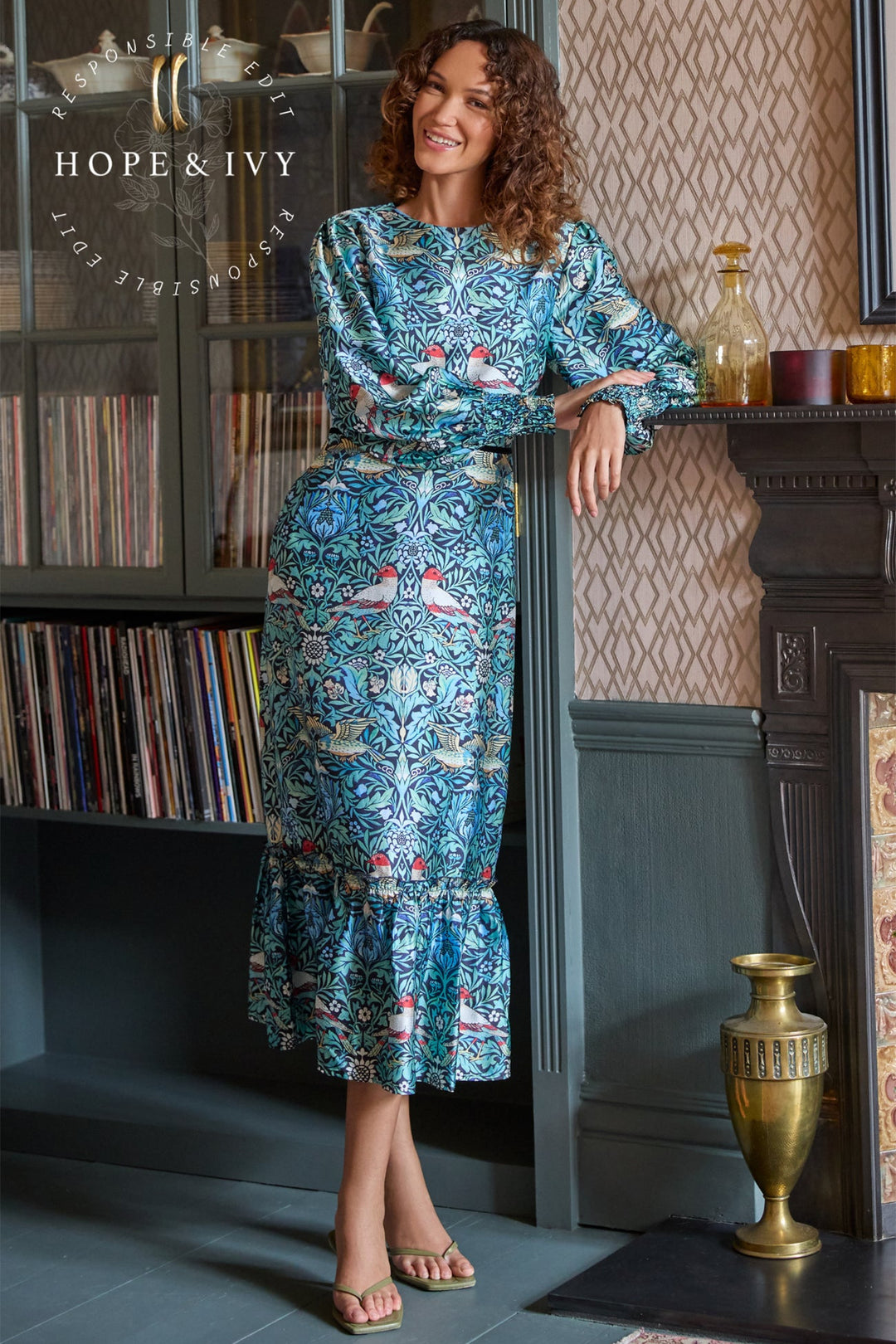 Woman in a blue patterned dress standing in a room with decorative elements.