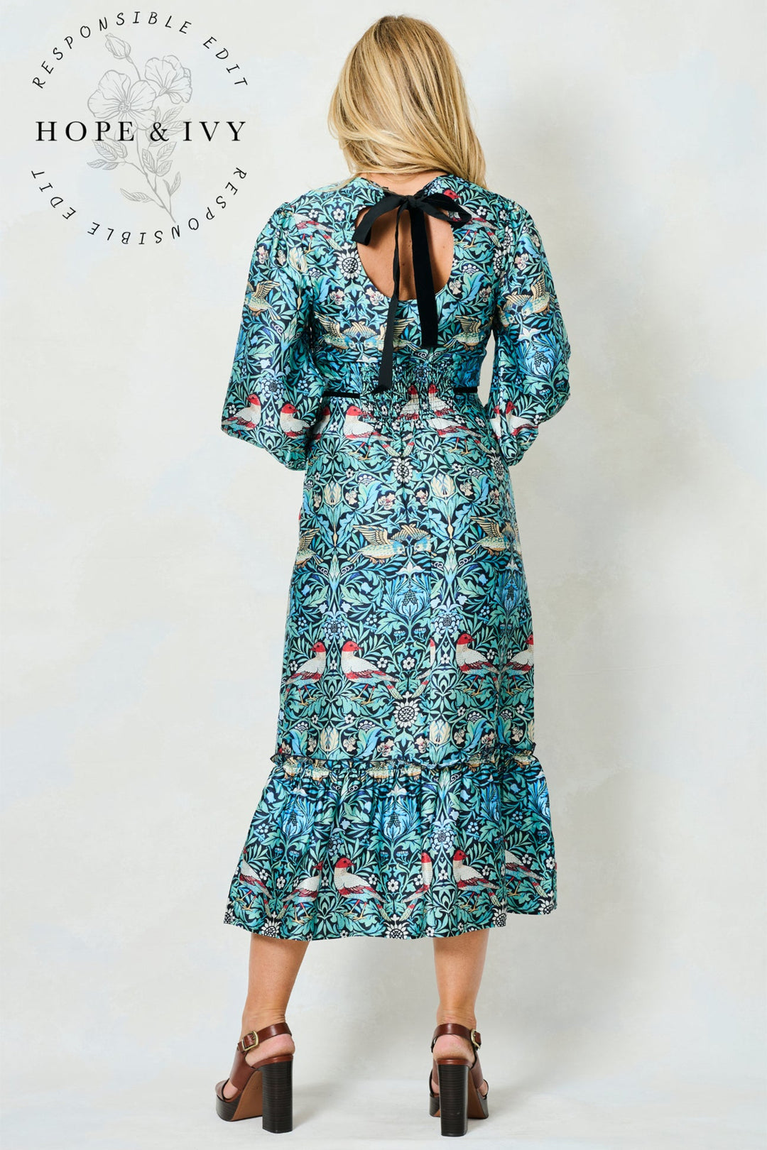 Woman wearing a patterned dress with a visible brand logo on a white background