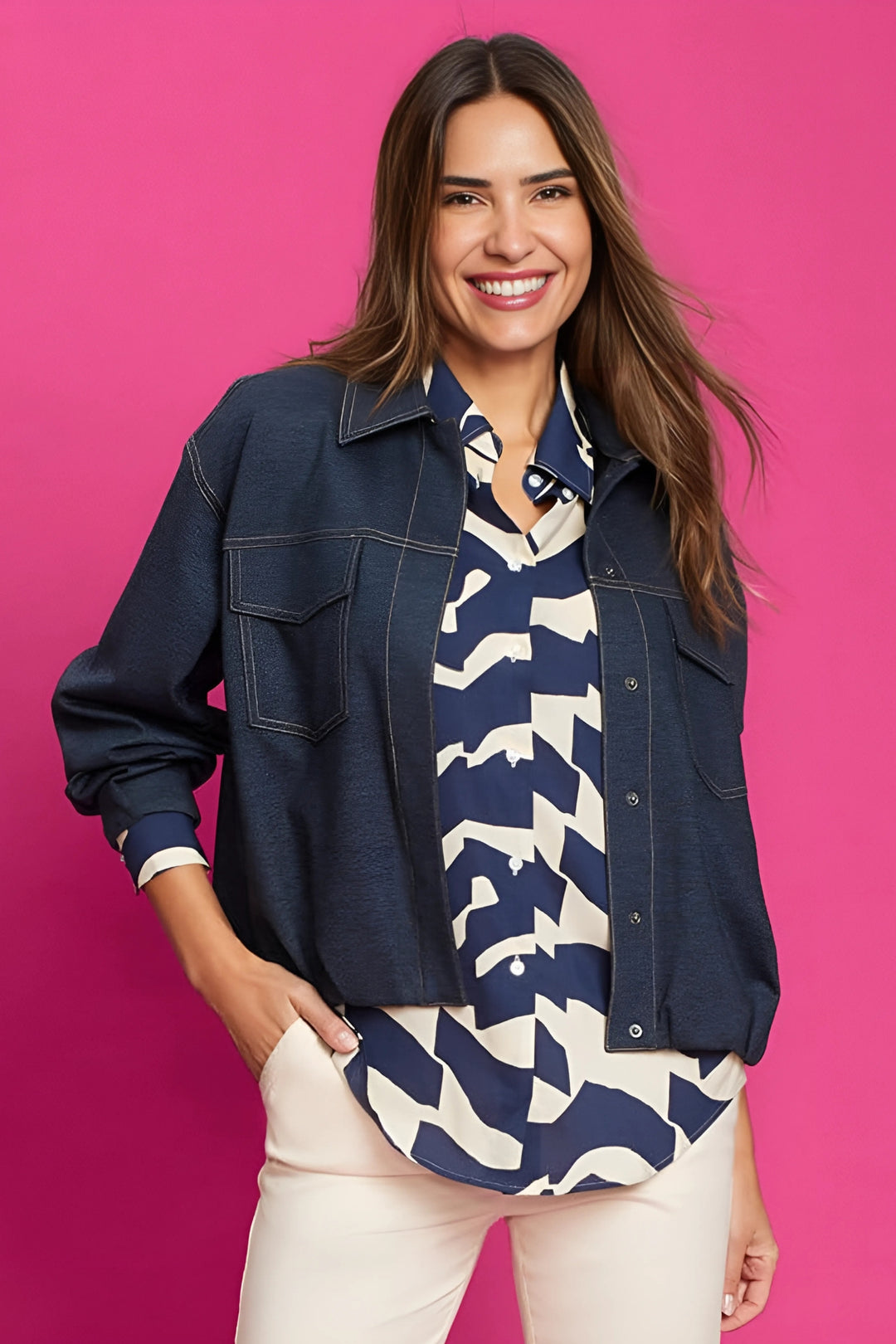 Woman wearing a navy denim jacket over a patterned shirt on a pink background