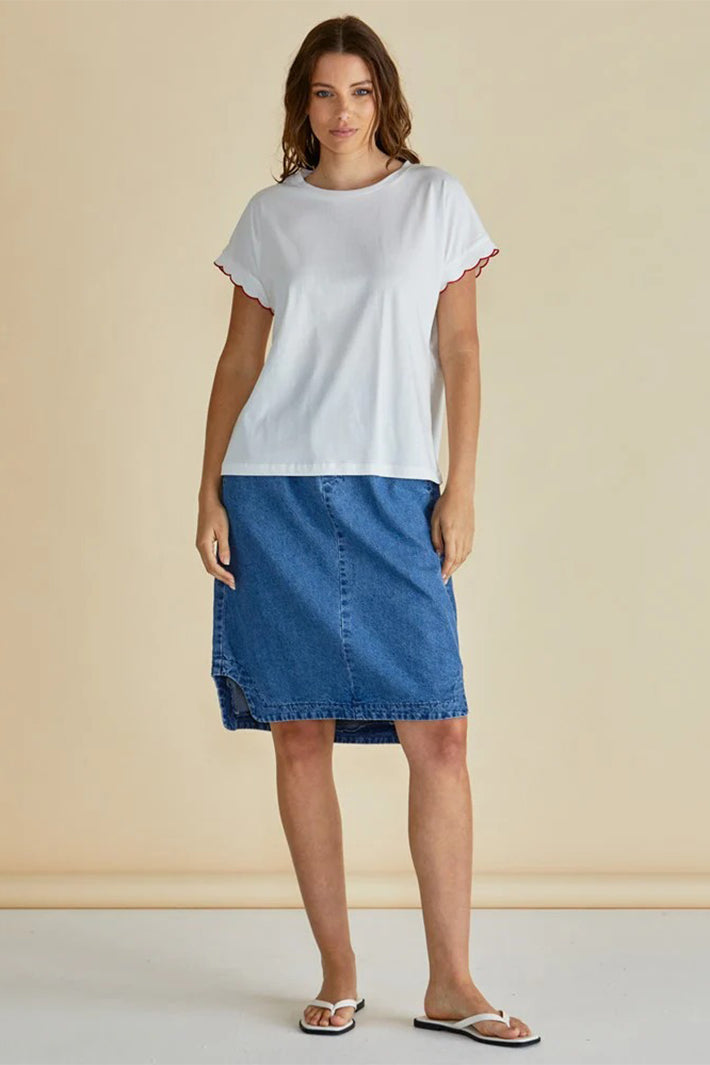 Woman wearing a white t-shirt and blue denim skirt against a beige background