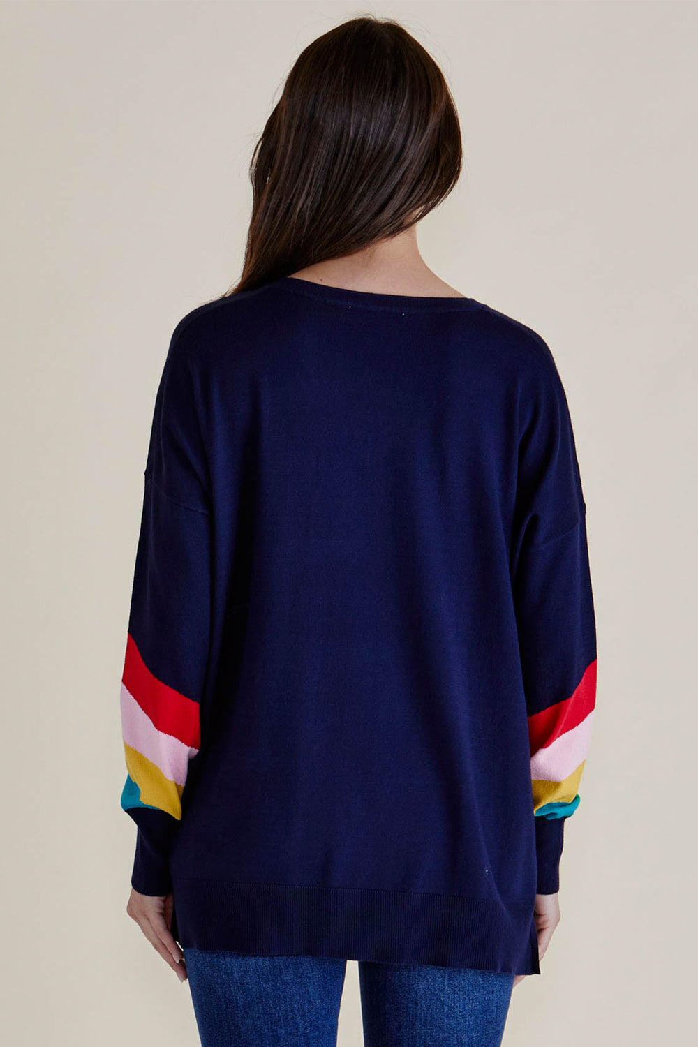 Navy sweater with colorful sleeves worn by a person on a beige background