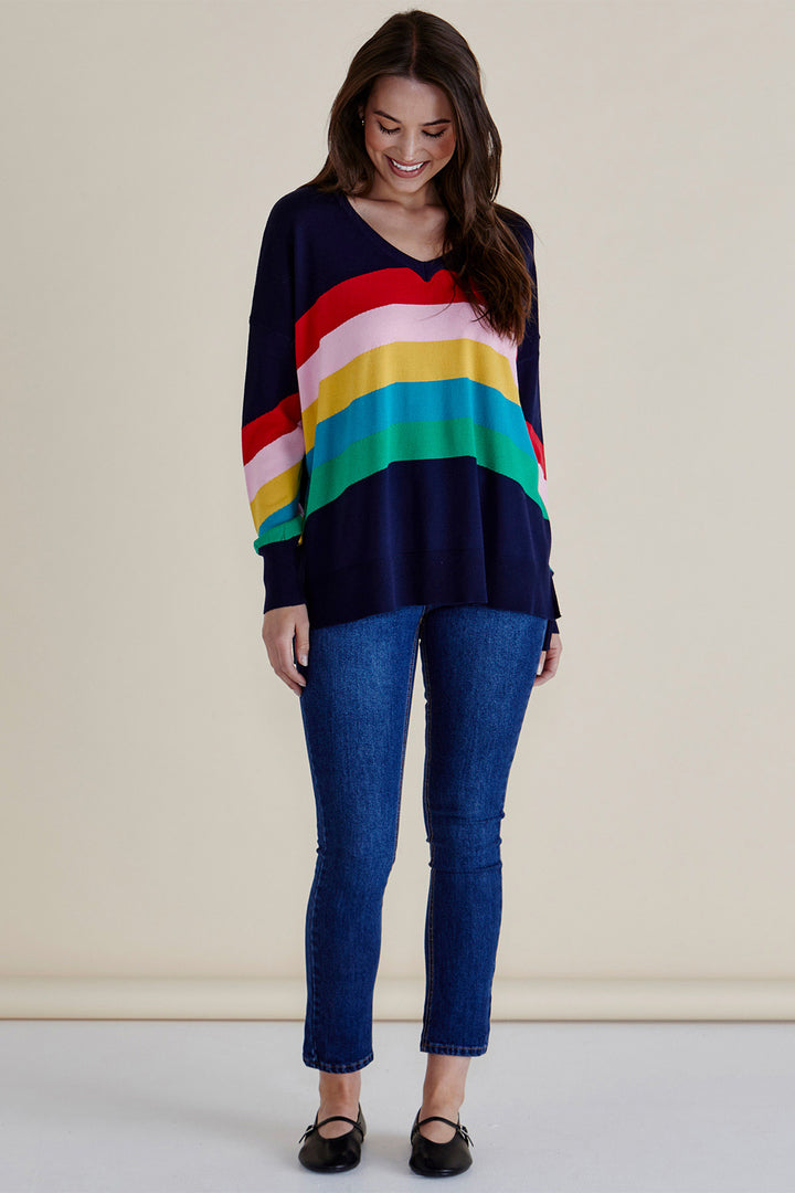 Woman wearing a colorful striped sweater and blue jeans against a beige background