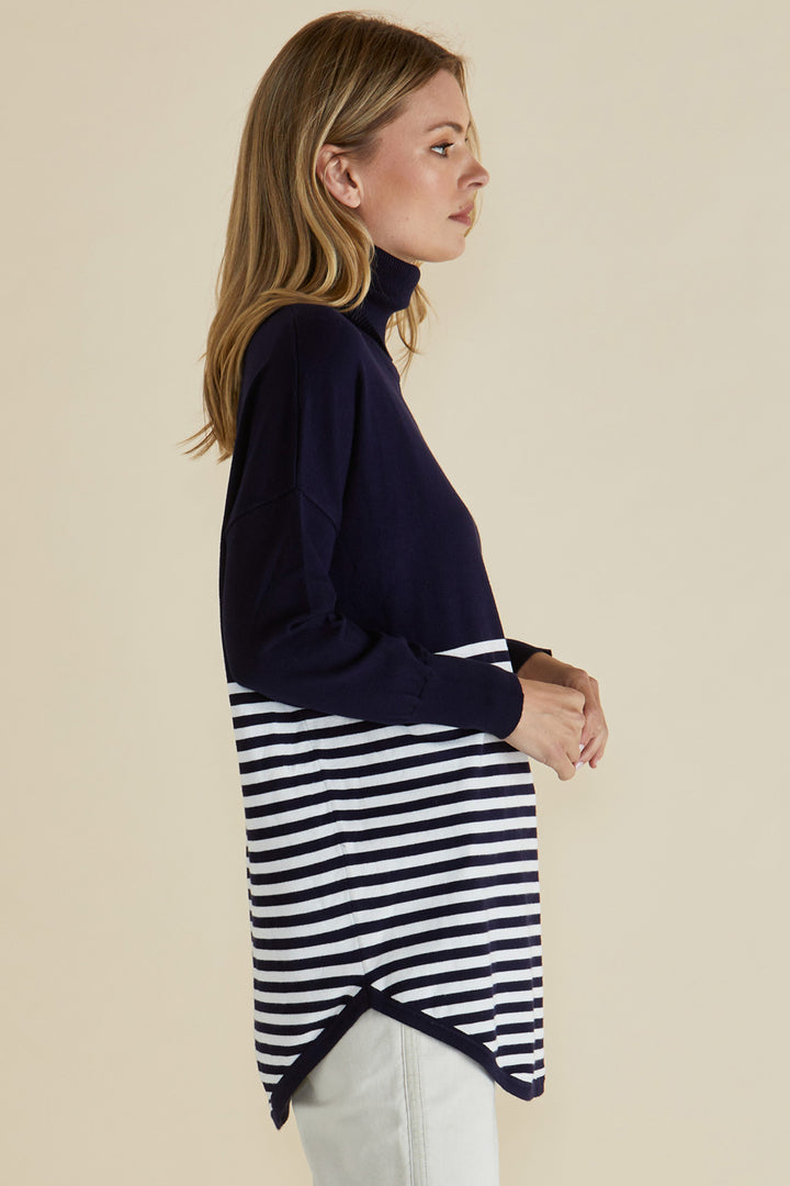 Woman wearing a navy sweater over a black and white striped skirt on a beige background