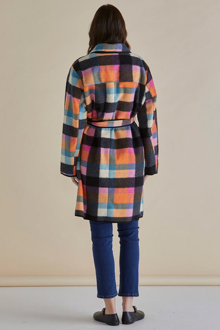 Person wearing a colorful plaid coat against a beige background