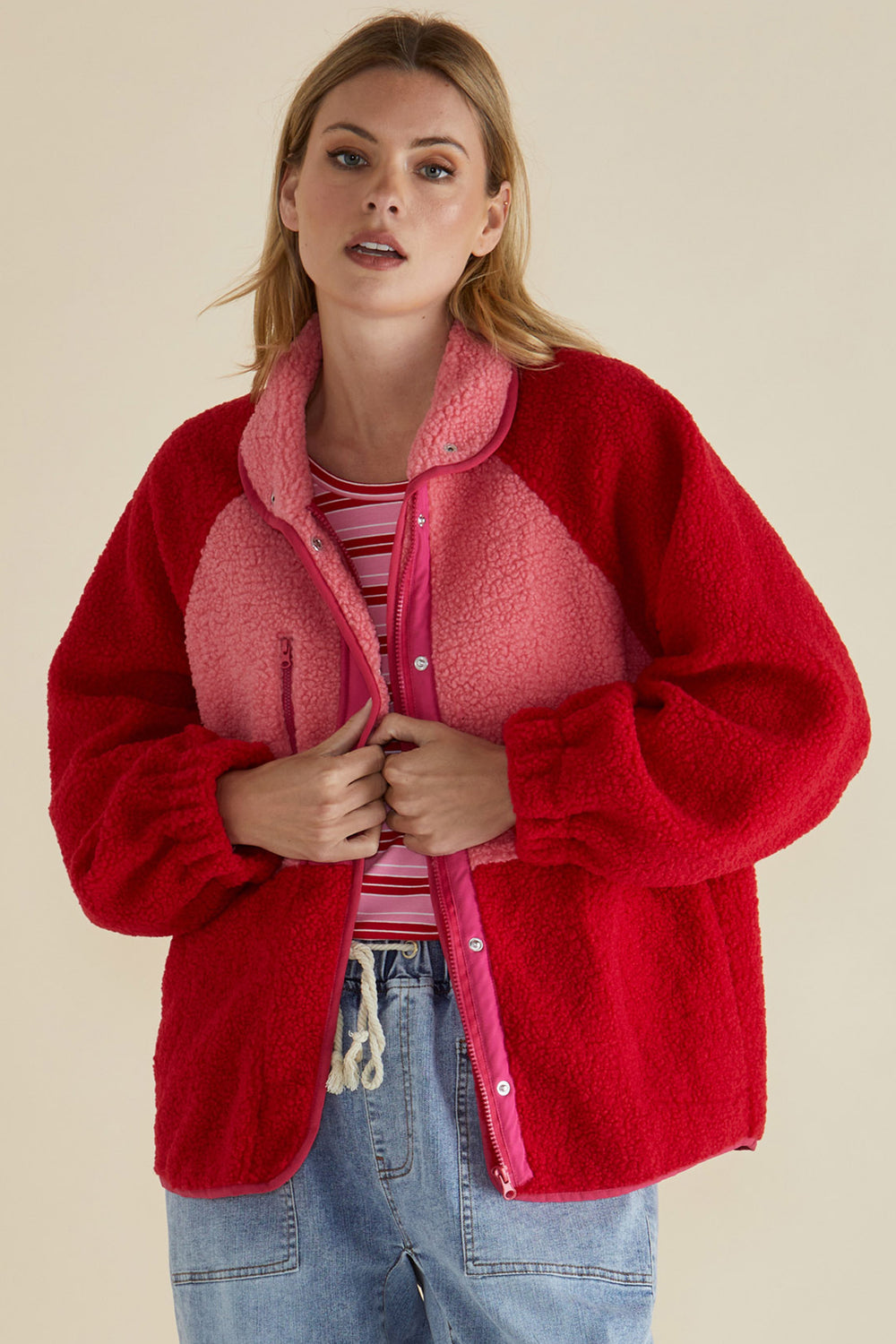 Woman wearing a red fleece jacket with pink interior on a beige background