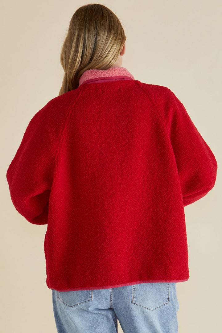 Person wearing a red cardigan and light blue jeans on a beige background