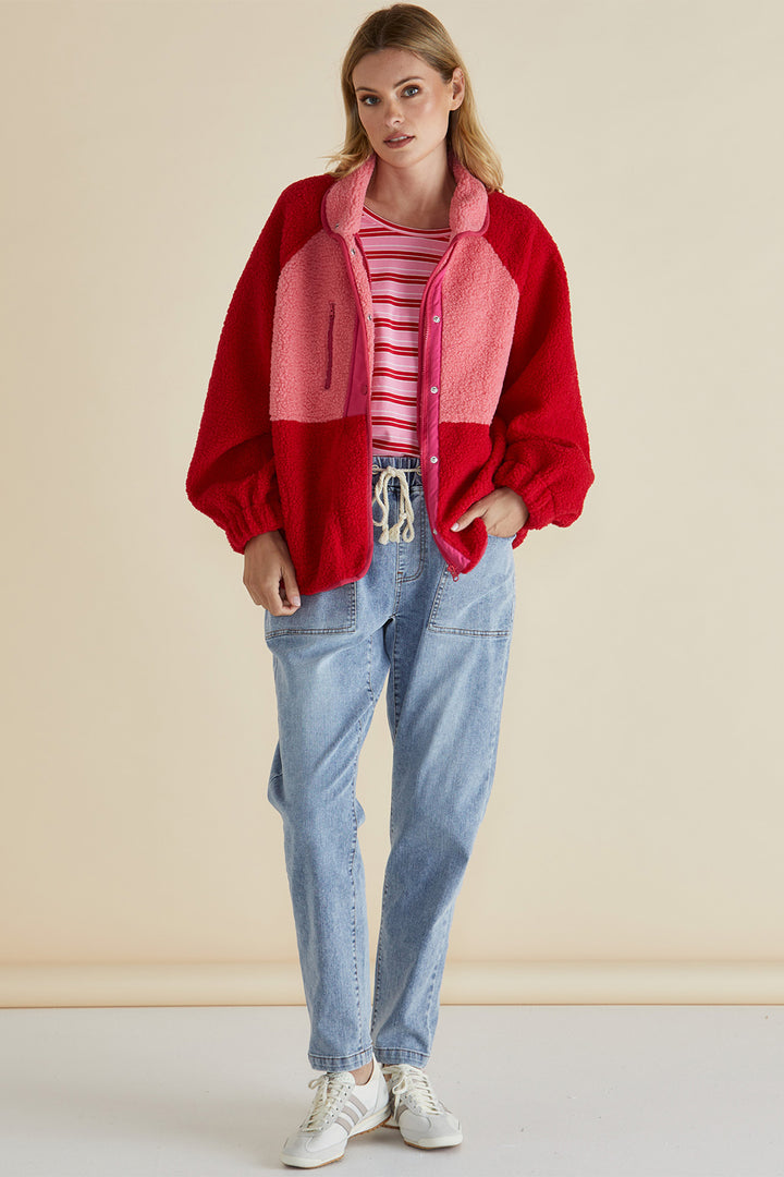 Woman wearing a red jacket, striped shirt, and blue jeans against a beige background