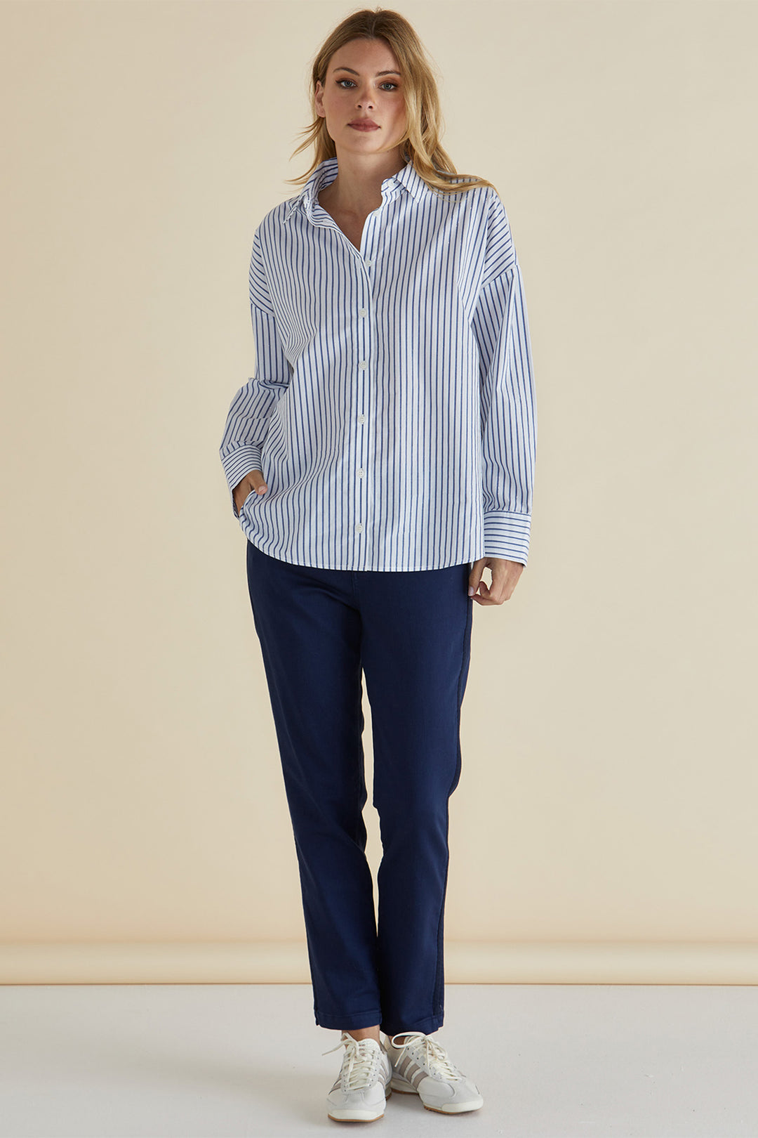 Woman wearing a blue and white striped shirt and navy pants against a beige background