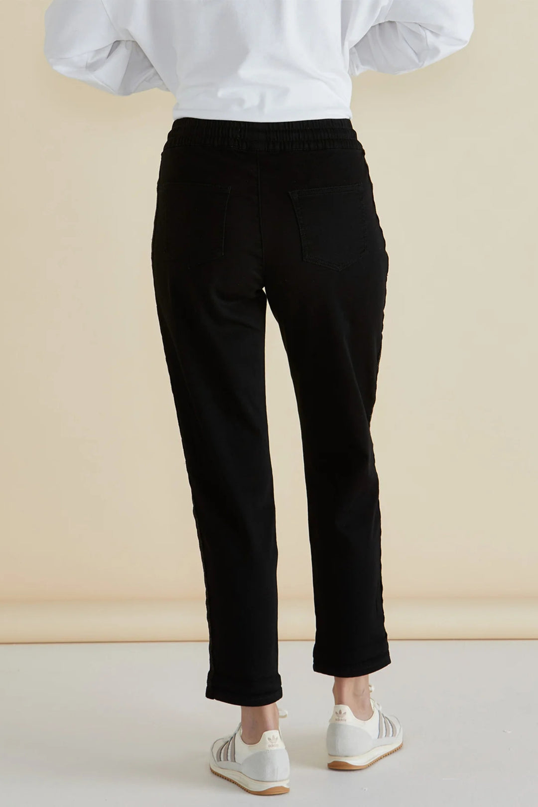 Person wearing black pants and a white top against a beige background